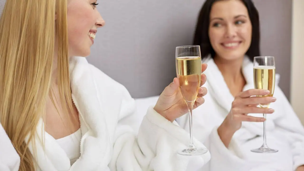 Duas amigas de roupão brindando com espumante em um dia de spa